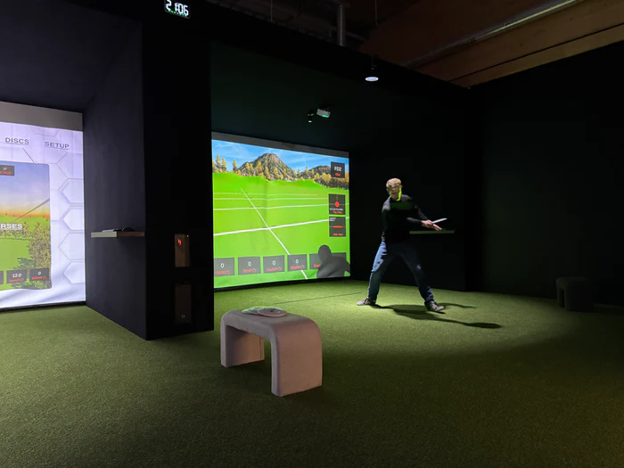 HYZR One indoor disc golf simulator bay — player mid-throw at the impact screen